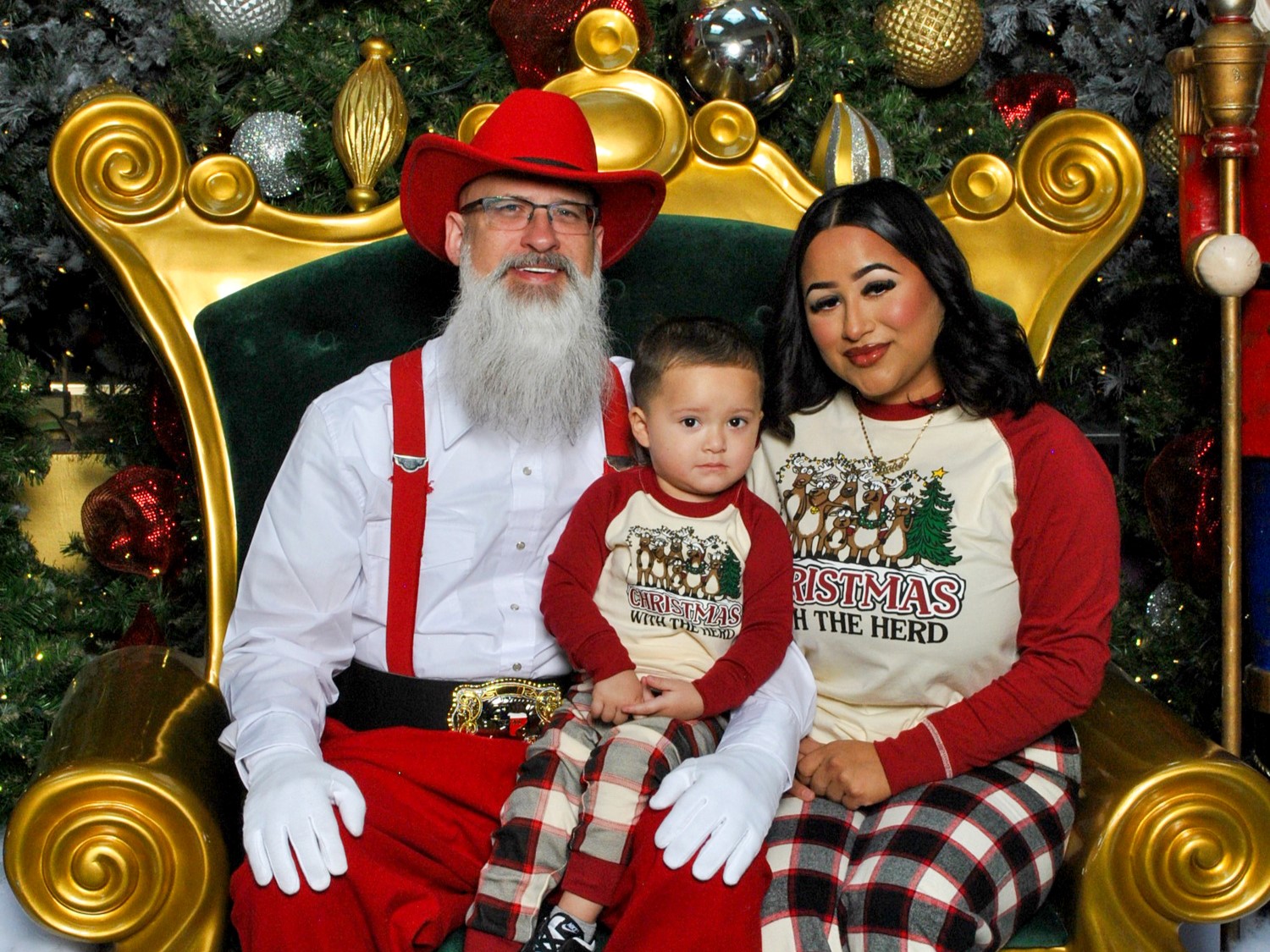 A person in a Santa costume sits on a golden throne, flanked by a child and an adult in matching festive attire, against a holiday backdrop.